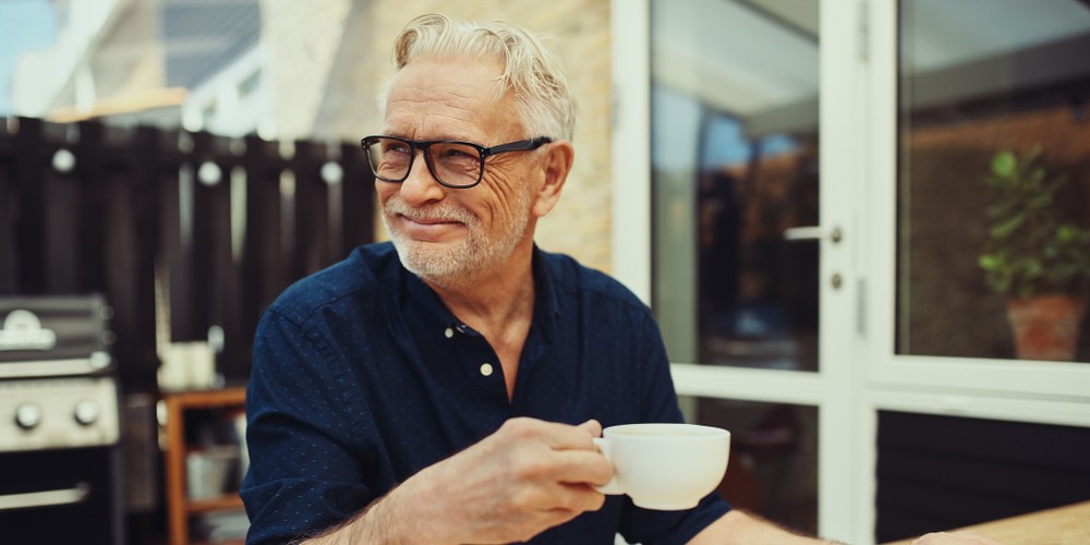 Smiling senior man drinking a cup of coffee and working online