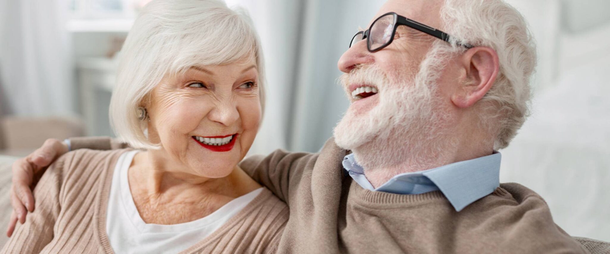 elderly couple smiling and sitting on a couch of their private senior apartment