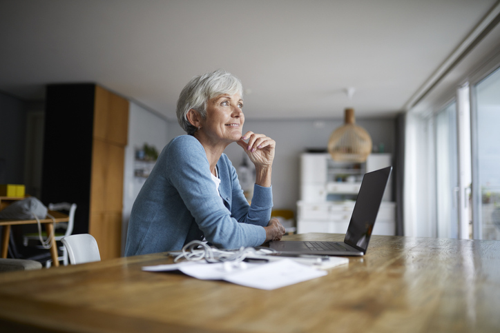 senior lady gazing through a window while working on a laptop