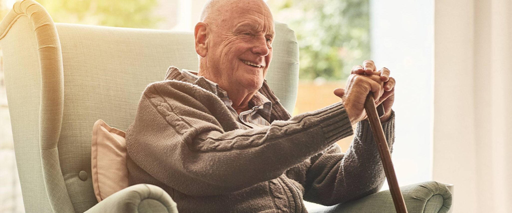 elderly man smiling while sitting on a chair with his cane in his hands