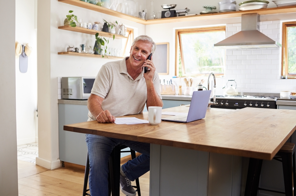 Happy senior man talking on the phone while using his laptop