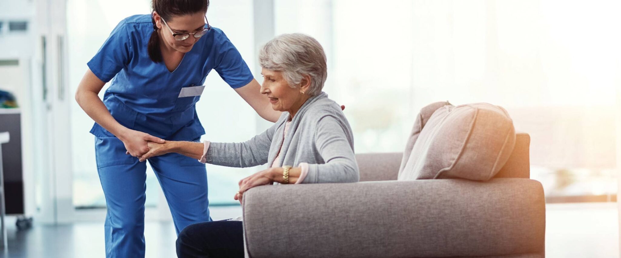 nurse helping assisted living resident get up off the couch