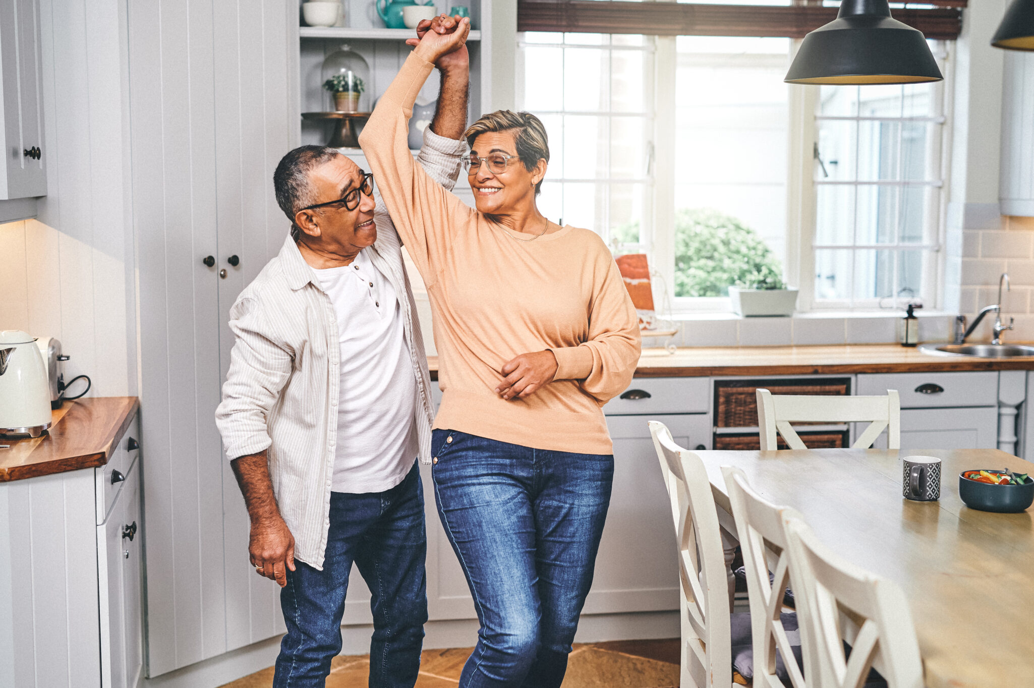 An older couple smile and do a twirl in the kitchen and dining room area