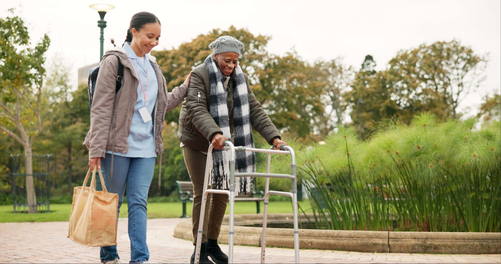 Senior woman walking outdoors with walker and female nurse